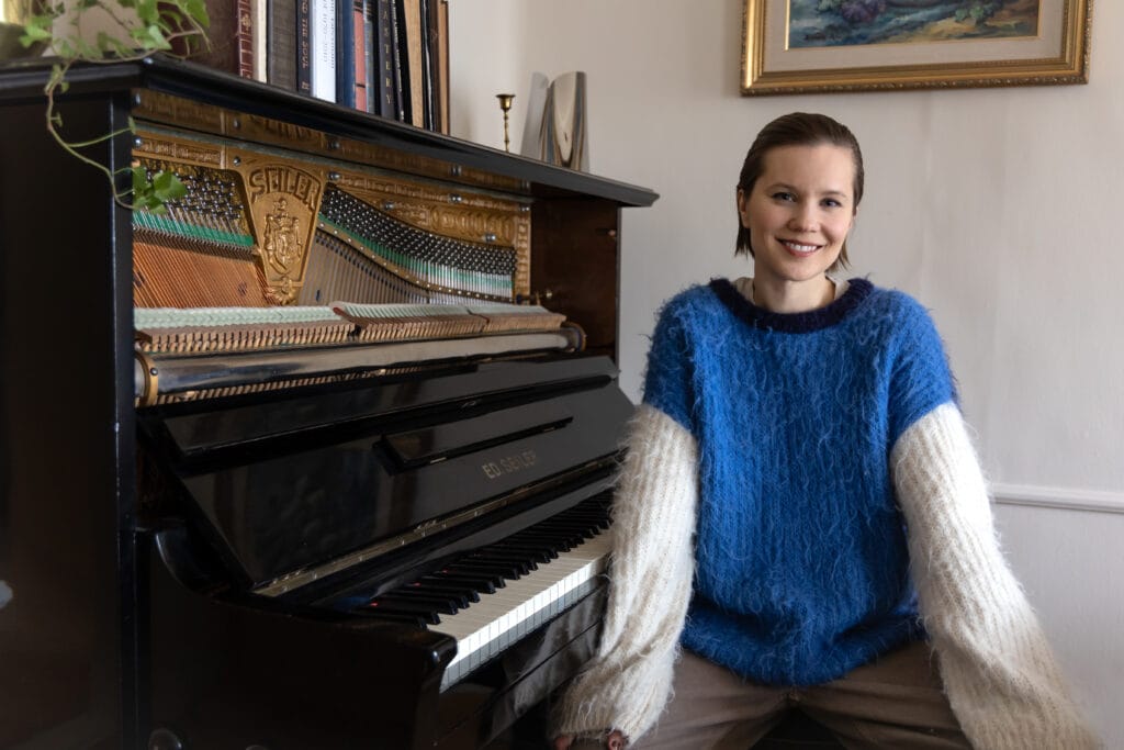 Bettina home at her piano looking at the camera.